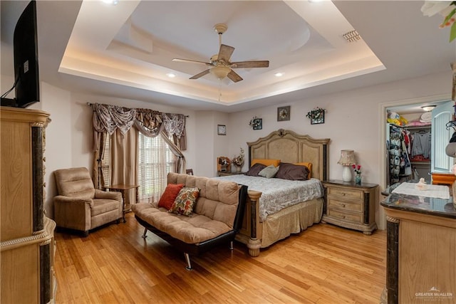 bedroom featuring light wood finished floors, visible vents, a raised ceiling, a ceiling fan, and a spacious closet