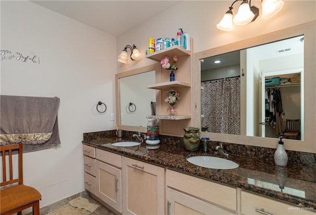 full bath with double vanity, visible vents, a walk in closet, and a sink