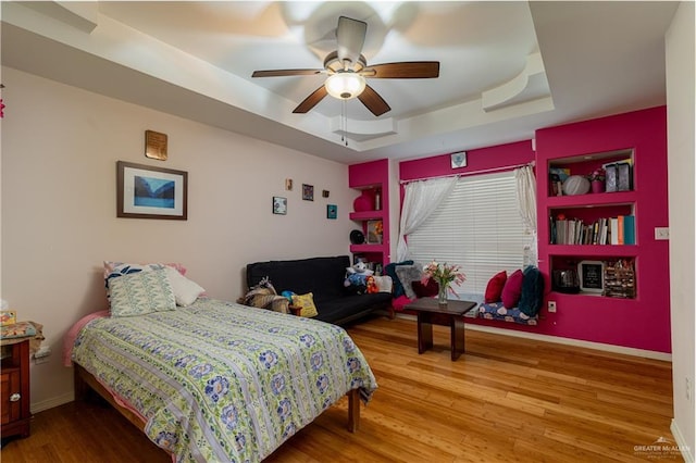 bedroom with ceiling fan, baseboards, a raised ceiling, and wood finished floors