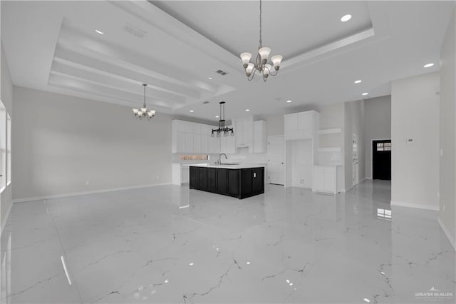 kitchen featuring a raised ceiling, white cabinetry, a kitchen island with sink, and an inviting chandelier