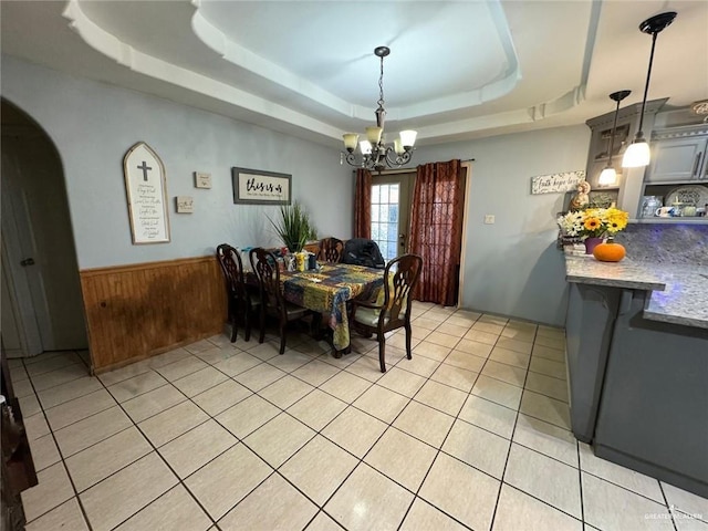 tiled dining area featuring wooden walls, a tray ceiling, and a notable chandelier