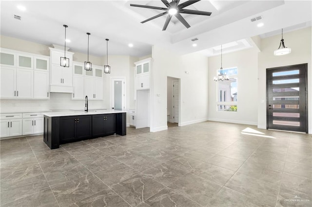 kitchen with ceiling fan with notable chandelier, decorative backsplash, an island with sink, decorative light fixtures, and white cabinetry