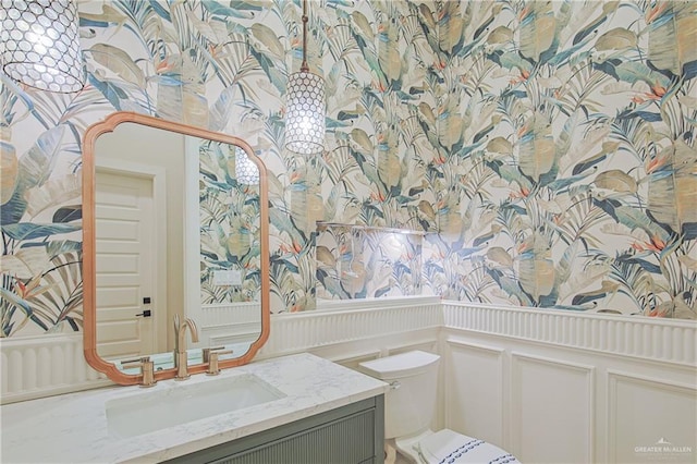 bathroom featuring toilet, a wainscoted wall, a decorative wall, and vanity