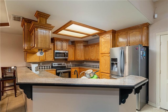 kitchen featuring kitchen peninsula, appliances with stainless steel finishes, backsplash, a kitchen breakfast bar, and light tile patterned flooring