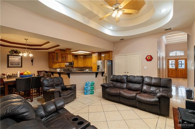 living room with a tray ceiling, light tile patterned flooring, and ceiling fan with notable chandelier