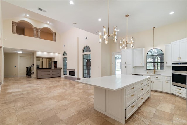 kitchen with a high ceiling, a center island, decorative light fixtures, and stainless steel double oven