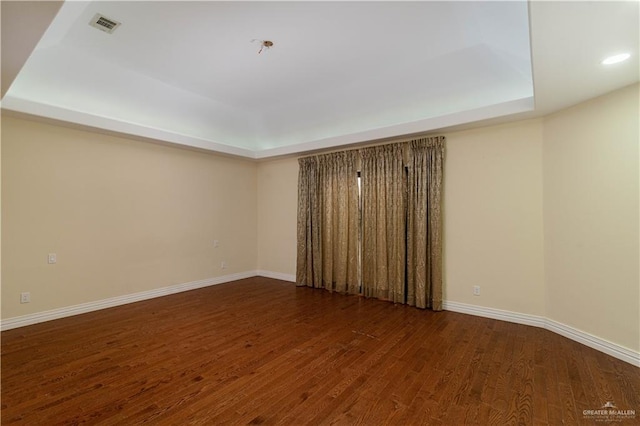 empty room with a tray ceiling and dark hardwood / wood-style flooring