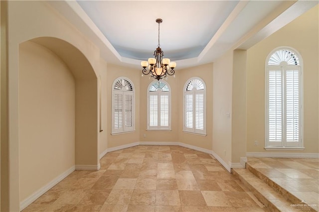 unfurnished dining area featuring a raised ceiling and an inviting chandelier