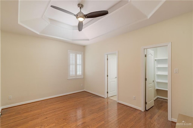 unfurnished bedroom featuring a spacious closet, ceiling fan, a raised ceiling, a closet, and hardwood / wood-style flooring