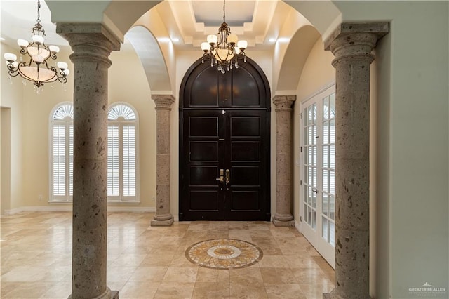 tiled entryway with french doors, a raised ceiling, a towering ceiling, a notable chandelier, and decorative columns