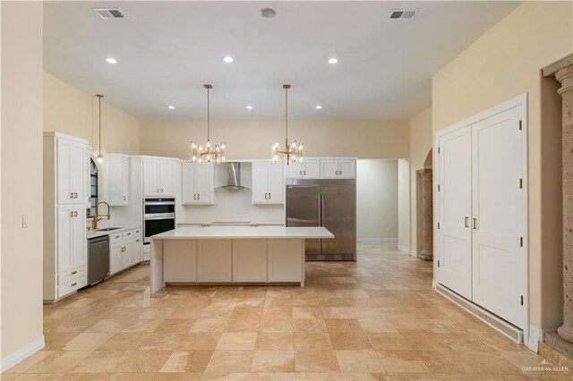 kitchen featuring stainless steel appliances, wall chimney range hood, pendant lighting, white cabinets, and a center island