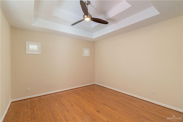 empty room featuring a tray ceiling, ceiling fan, and light hardwood / wood-style flooring