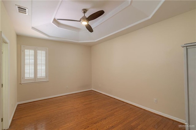 unfurnished room with ceiling fan, wood-type flooring, and a tray ceiling