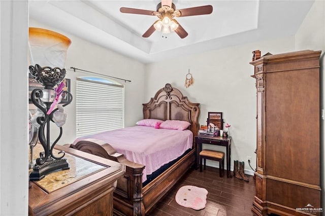 bedroom featuring a tray ceiling, a ceiling fan, dark wood-style floors, and baseboards