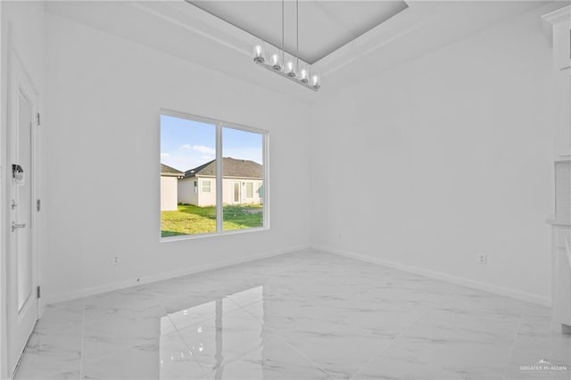 empty room featuring marble finish floor, a raised ceiling, a notable chandelier, and baseboards