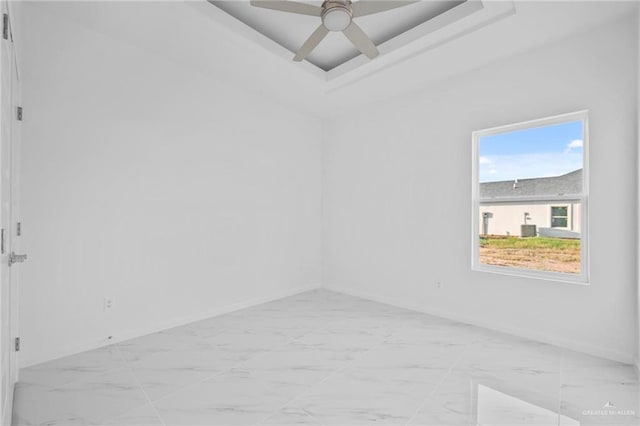 empty room featuring baseboards, marble finish floor, a tray ceiling, and a ceiling fan