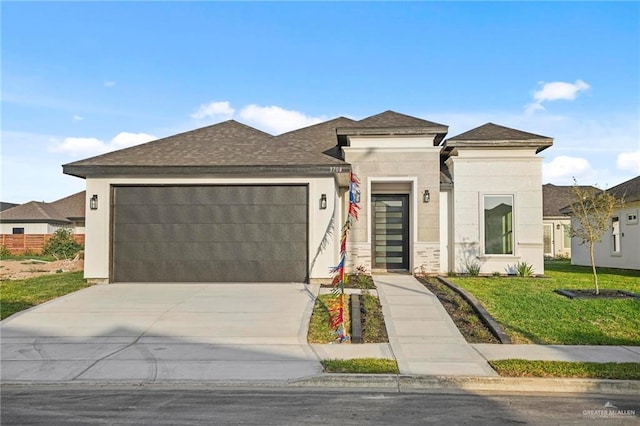 prairie-style home with a shingled roof, driveway, a front lawn, and an attached garage