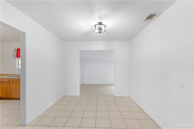 unfurnished room with light tile patterned flooring, sink, and a textured ceiling