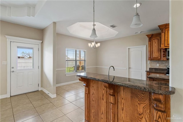 kitchen featuring light tile patterned floors, a notable chandelier, pendant lighting, dark stone counters, and decorative backsplash