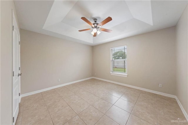 tiled empty room featuring a raised ceiling and ceiling fan