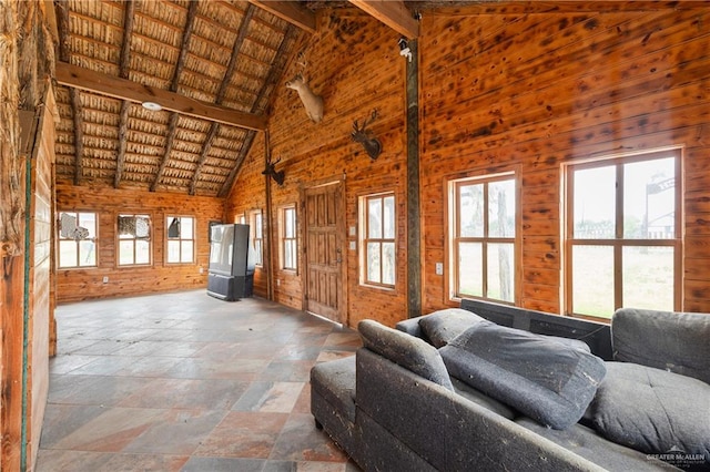 unfurnished living room featuring a wealth of natural light, wooden walls, and high vaulted ceiling