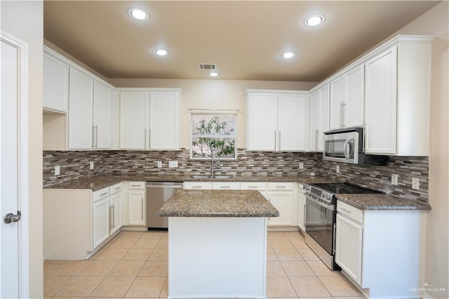 kitchen with a center island, white cabinets, dark stone countertops, appliances with stainless steel finishes, and light tile patterned flooring