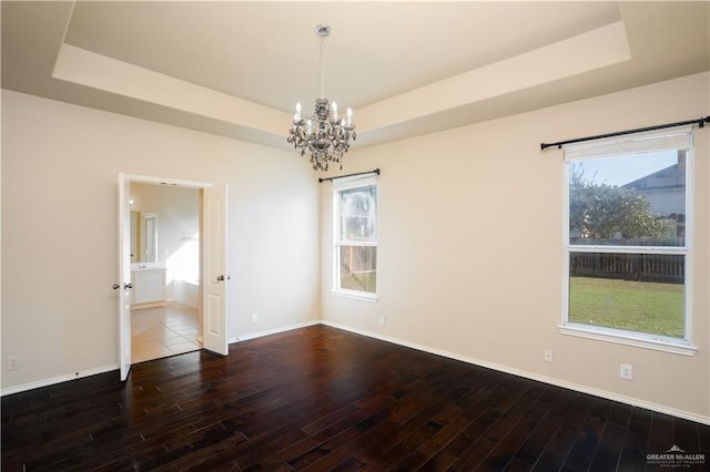 spare room featuring wood-type flooring, an inviting chandelier, a raised ceiling, and a healthy amount of sunlight