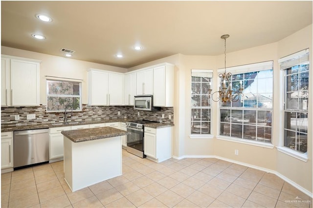 kitchen featuring dark stone counters, stainless steel appliances, light tile patterned floors, a center island, and white cabinetry