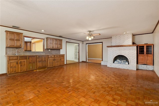 unfurnished living room with crown molding, ceiling fan, a brick fireplace, and light parquet floors