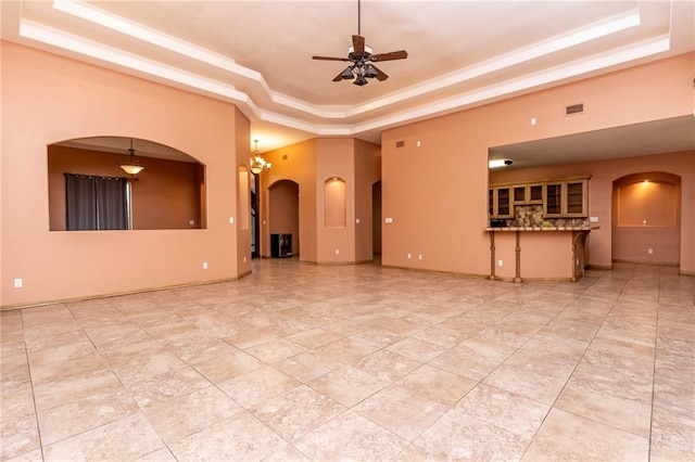 unfurnished living room featuring a tray ceiling and ceiling fan with notable chandelier