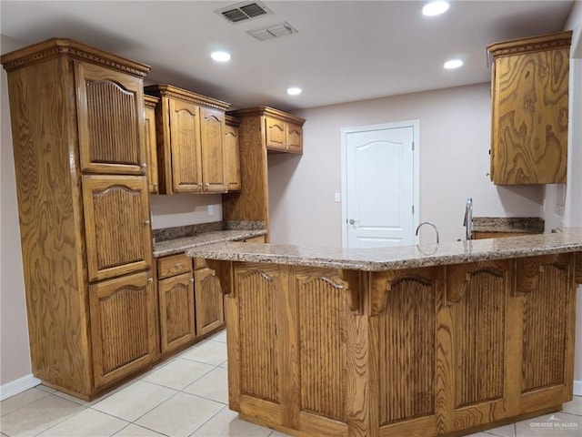 kitchen with kitchen peninsula, light stone countertops, and light tile patterned floors