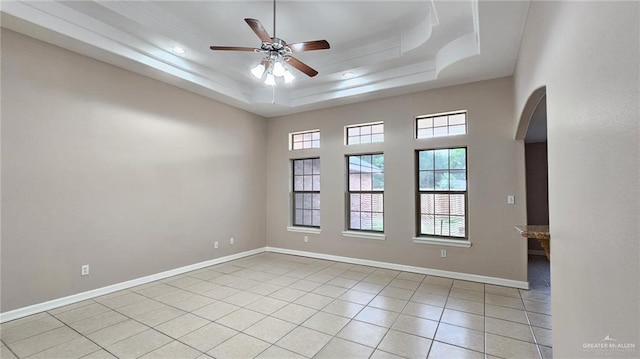 empty room featuring a raised ceiling, ceiling fan, and light tile patterned flooring