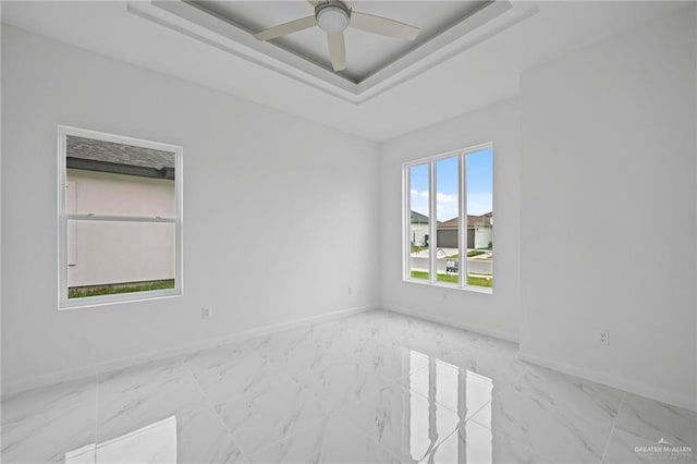 unfurnished room featuring a tray ceiling, baseboards, marble finish floor, and ceiling fan