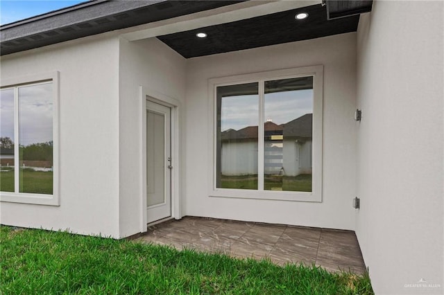 view of exterior entry with stucco siding and a patio