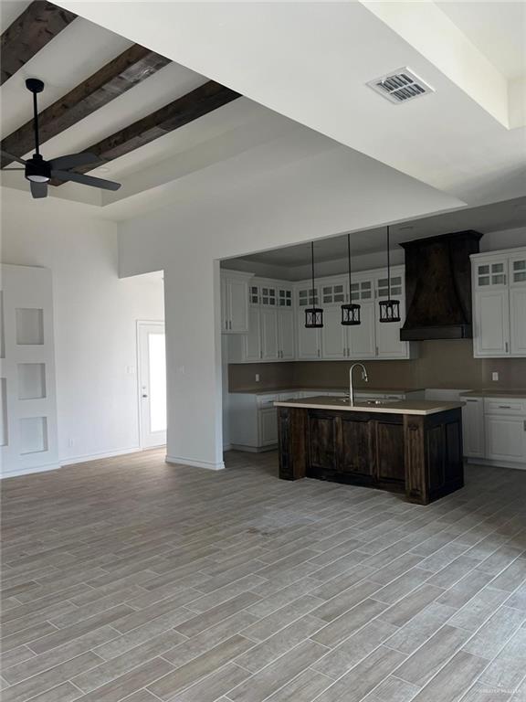 kitchen featuring ceiling fan, light hardwood / wood-style floors, a kitchen island with sink, white cabinets, and custom range hood