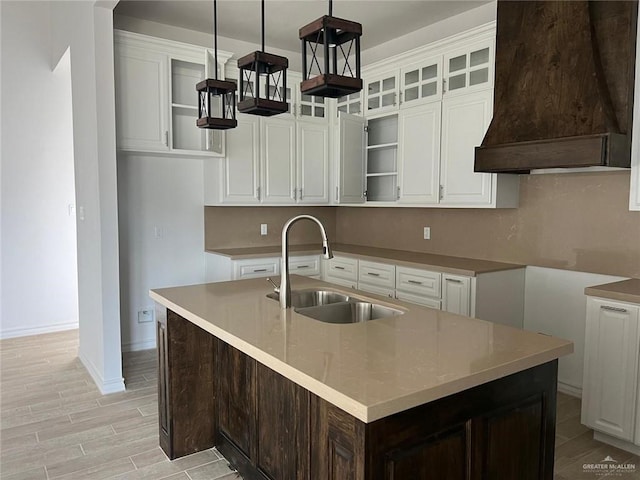 kitchen featuring a kitchen island with sink, sink, hanging light fixtures, and custom exhaust hood