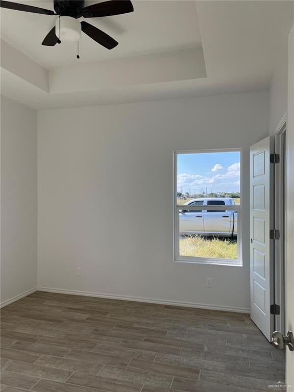 empty room with ceiling fan, dark hardwood / wood-style flooring, and a tray ceiling