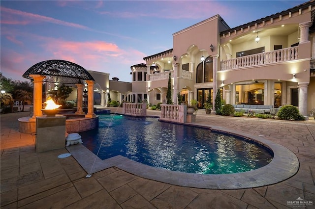 pool at dusk with a pool with connected hot tub, a patio area, and a gazebo