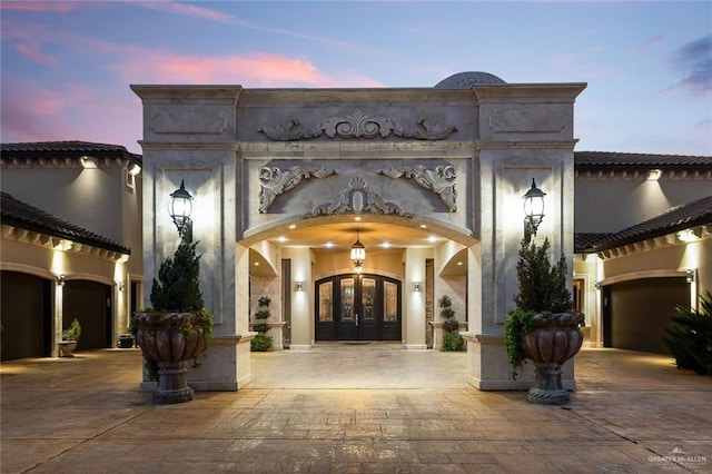 exterior entry at dusk featuring a garage, concrete driveway, and french doors