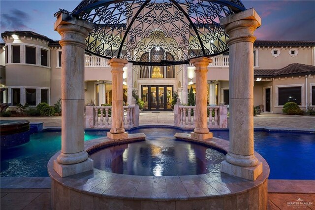 pool at dusk featuring a pool with connected hot tub and a patio