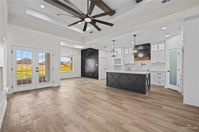 kitchen with a kitchen island with sink, ceiling fan with notable chandelier, hanging light fixtures, light hardwood / wood-style flooring, and white cabinetry