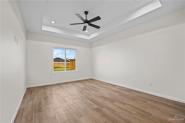 empty room with a tray ceiling, ceiling fan, and light wood-type flooring