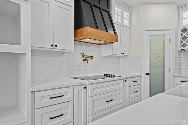 kitchen featuring tasteful backsplash, white cabinetry, premium range hood, and black electric cooktop