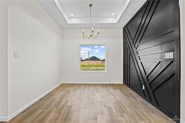 empty room featuring an inviting chandelier, light wood-type flooring, and a tray ceiling