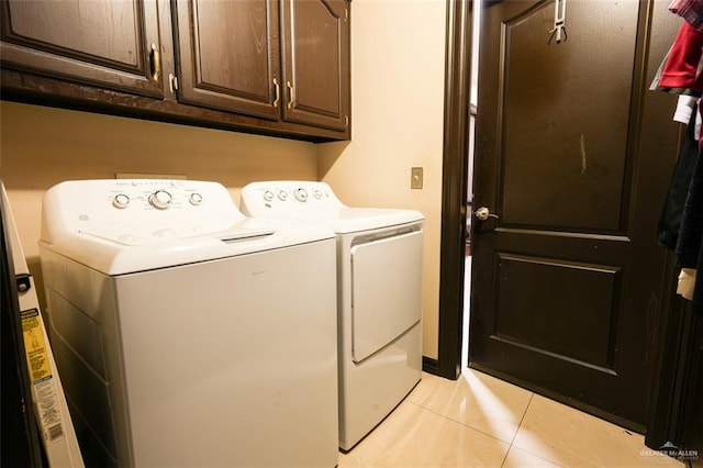 laundry area featuring washing machine and clothes dryer, light tile patterned floors, and cabinets