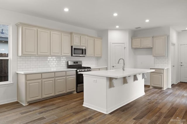 kitchen featuring a kitchen island with sink, cream cabinets, dark wood-type flooring, and stainless steel appliances