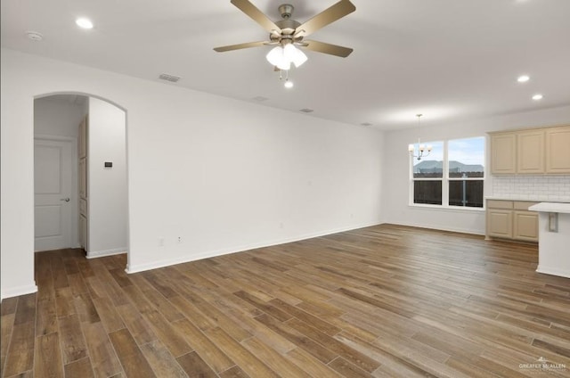 unfurnished living room featuring hardwood / wood-style floors and ceiling fan with notable chandelier