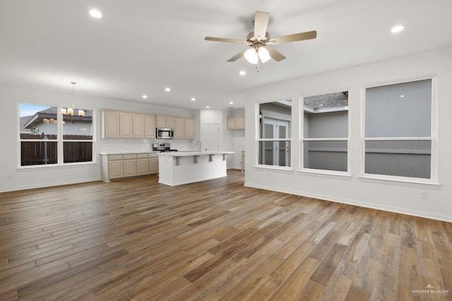 unfurnished living room featuring hardwood / wood-style flooring, sink, and ceiling fan with notable chandelier