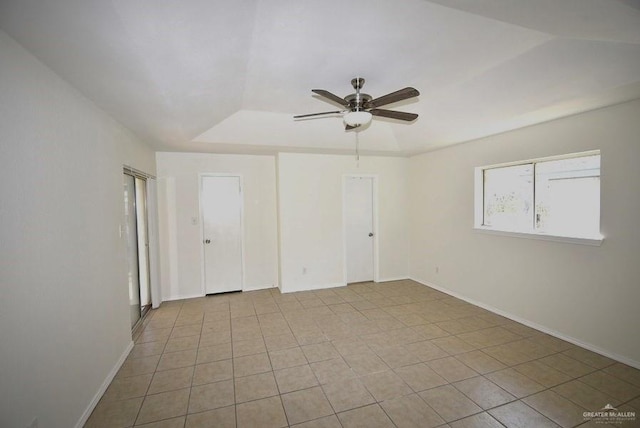 unfurnished room with a raised ceiling, light tile patterned floors, a ceiling fan, and baseboards