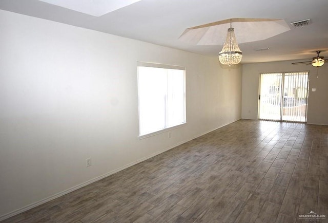 empty room with dark wood-style floors, visible vents, ceiling fan with notable chandelier, and baseboards